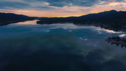 Golden sunrise over lake with glowing clouds and mountains reflected on calm morning water surface