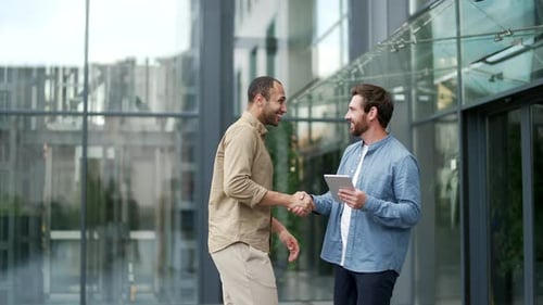 Two businessmen shaking hands outside modern office building, symbolizing successful business