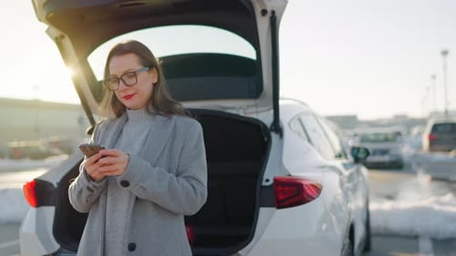 Woman Uses Phone Next to Car in Parking Lot