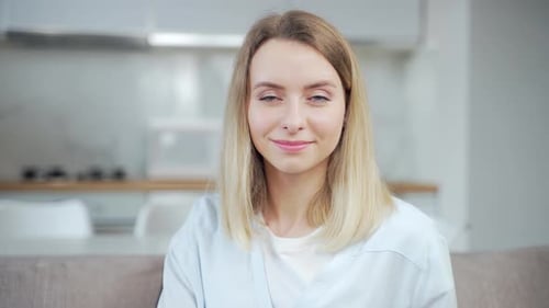 Close-up portrait of young beautiful blonde woman at home on kitchen background looking at camera.