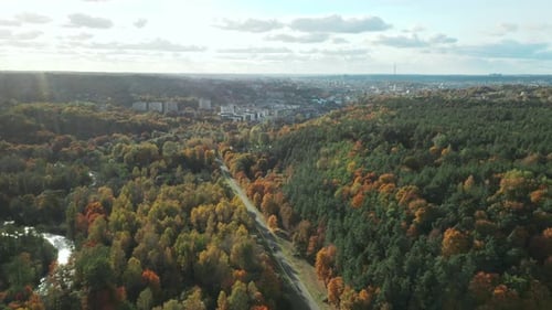 AERIAL: Vilnius city Panorama with cars driving on road through autumn yellow forest covered with fi