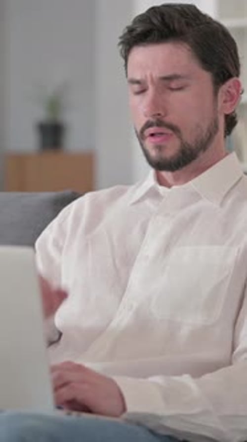Man Working on Laptop Expressing Headache Pain Indoors