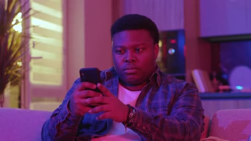 Young Man Uses Mobile Phone on Sofa at Home