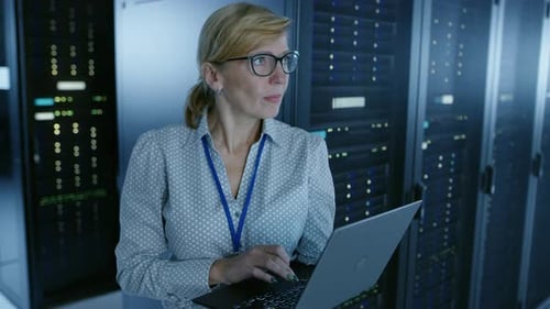 In Data Center: Female IT Technician Running Maintenance Programme on a Laptop, Controls Operationa