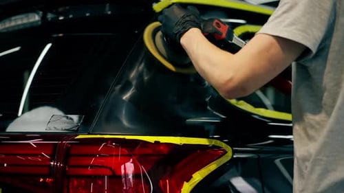 Autodetails an einer Tankstelle Das schwarze Auto ist mit gelbem Klebeband bedeckt, der Prozess des Polierens
