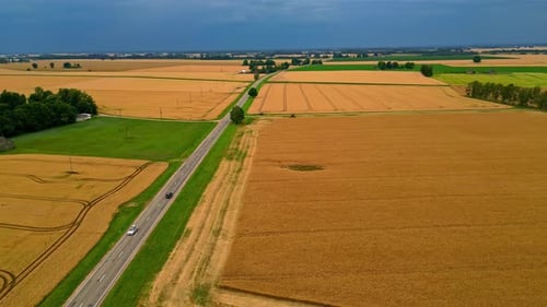 Pan shot of a highway passing through agriculture fields on a cloudy day. Aerial view.