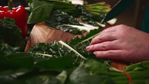 Les mains d'une femme coupent des feuilles d'épinards de betterave argentée sur une planche à découper en bois dans la cuisine, préparant des aliments sains