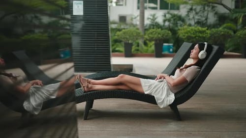 Woman Relaxing on a Lounger Listening to Music with Headphones in a Garden