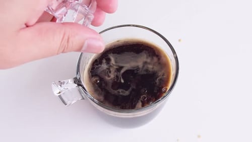 Close-up coffee black pouring iced into a drinking glass on white background. Slowmotion