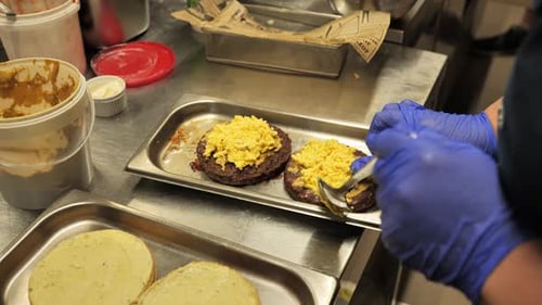 Assemblage de hamburgers de cuisine professionnel : les mains ajoutent de la sauce à des galettes juteuses 4K