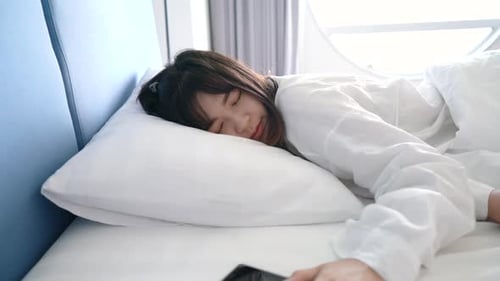 Asian woman waking up and sleep with smartphone alarm clock her walking look a sea