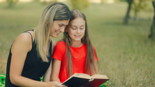 Joyful Mother and Daughter Reading Barefoot in a Grassy Park