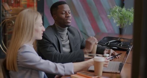 Business Partners Caucasian Woman and African American Man Talking Looking at Laptop Screen in Cafe