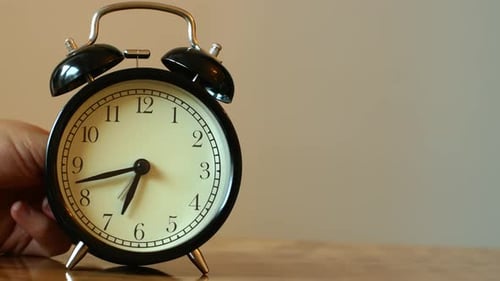A woman's hand turns off the ringing desk clock. The early rise of the alarm clock.