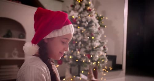 Girl Opens Christmas Gift by Sparkling Tree