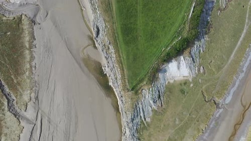 Aerial top down view of the shoreline around a grassy hill at low tide, on bright sunny day.
