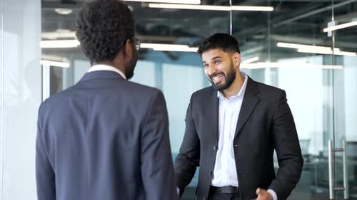 Happy businessmen in formal suits greeting each other with handshake in office lobby.