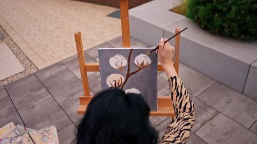 A young girl artist paints a picture with a brush on a canvas that stands on an easel view behind