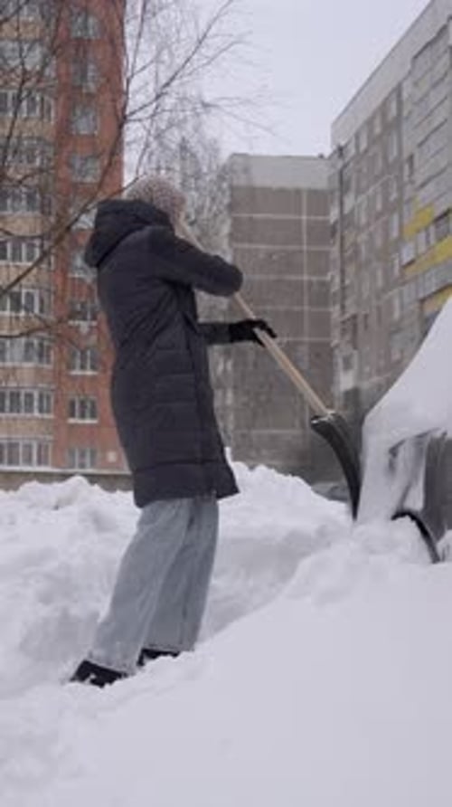 Woman shovels snow from car in winter landscape