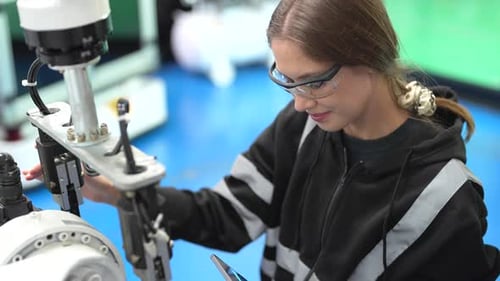 Female technician programs a robot arm with a digital tablet and assembly robot in a factory. Appren