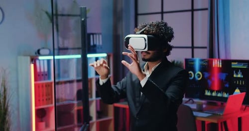 Attractive man in suit wearing augmented reality goggles working on imaginary screen in office