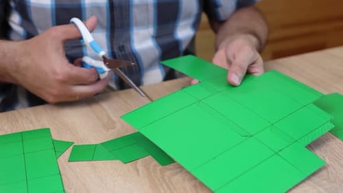 Man Cutting Green Paper to Make Geometric Box