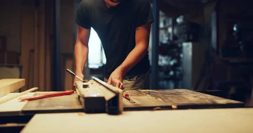 Male carpenter uses table saw to cut wood in factory atelier