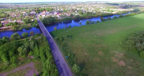 Blue river separating the village from farmlands. Little concrete bridge over the river.