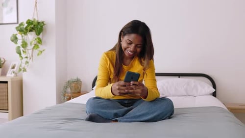Smiling Woman Using Phone on Bed in Bedroom