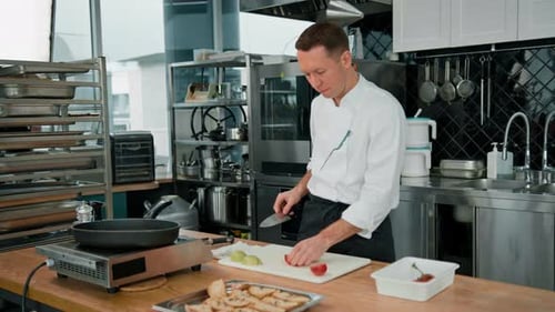 Professional kitchen chef slicing fresh juicy red tomato with a knife close-up vegetables on table