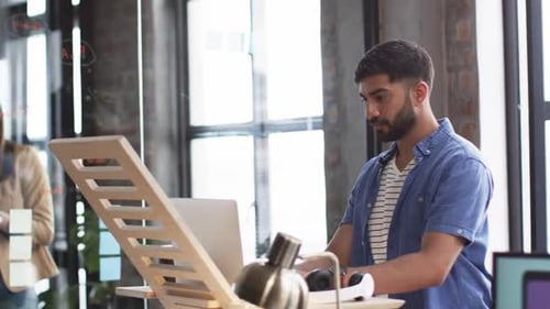Asian man works by drawing board, woman smiles, in a casual office.