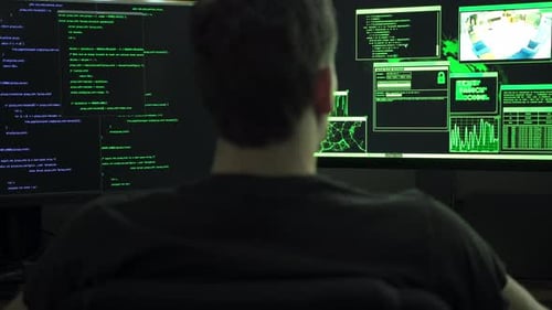 Male computer hacker sitting in front of computer monitors typing code.