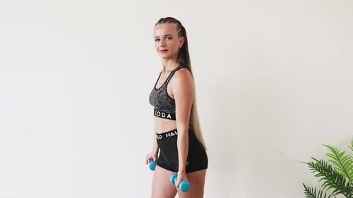 Young Woman Exercising with Dumbbells on a Bright Background