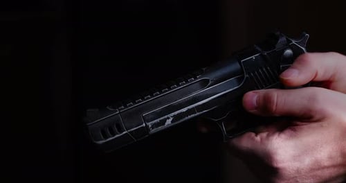 Hand Holding Black Gun Weapon Against Dark Background