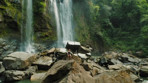 Woman exploring giant rocks and cascading waterfalls in Costa Rican forest
