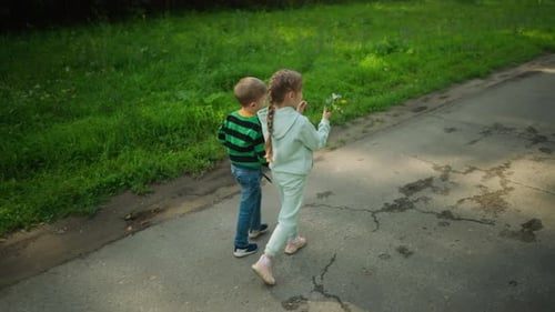 Children Walking Along Tarred Path on Sunny Day with Flower in Hand