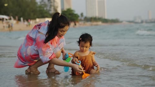 happy toddler baby girl playing toy and water with her mother on the sea beach