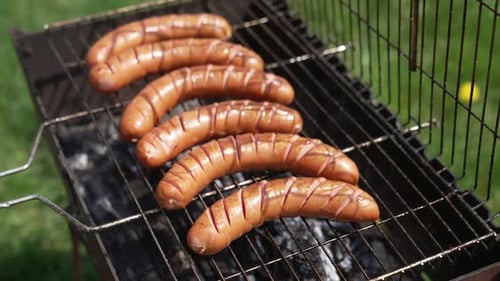 Hot dog sausages roasting in smoke. Chef opens grill grate and turns over juicy sausages.