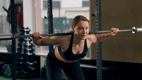 in the Gym Girl Trainer in a Black Top is Standing Doing Exercises with a Barbell