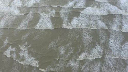 Top-down aerial shot of the blue ocean waves crashing on the shore.