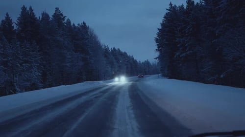 Winterschneesturm auf dem Highway in der Dämmerung Der Schneesturm wirbelt heftig über Asphaltstraßen, Pinien und Tannen
