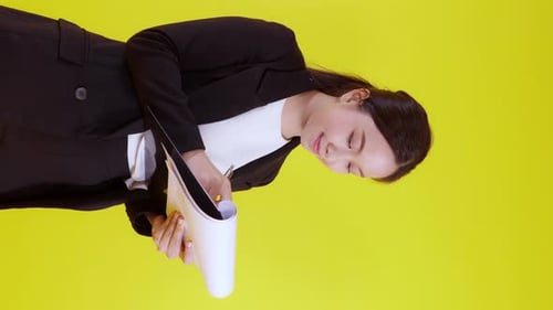 Portrait young asian businesswoman hold and writing note on clipboard isolated on yellow background.