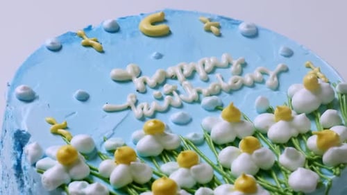 Zooming out of a close-up shot of a blue frosted birthday cake, decorated with small white flowers w