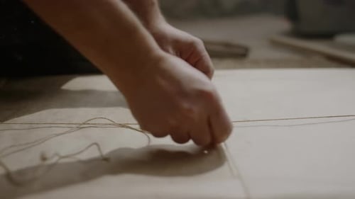 Unerkennbarer Handwerker beim Binden von Gemälden, in Papier eingewickelt, mit Schnur
