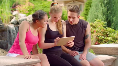 Three friends look at tablet near water feature