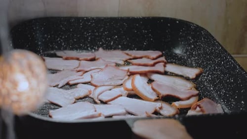 The Cook Stirs the Frying Bacon with a Spoon Camera Follows Cooking Bacon on Grill