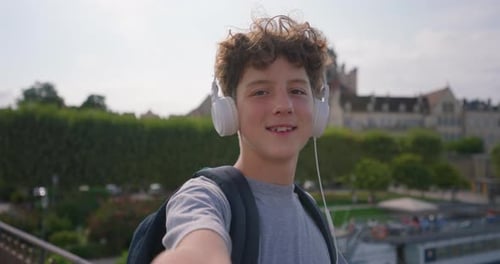 A Cute Teenager Tourist in Headphones Walks Around the City and Shoots His Happy Face on the Phone