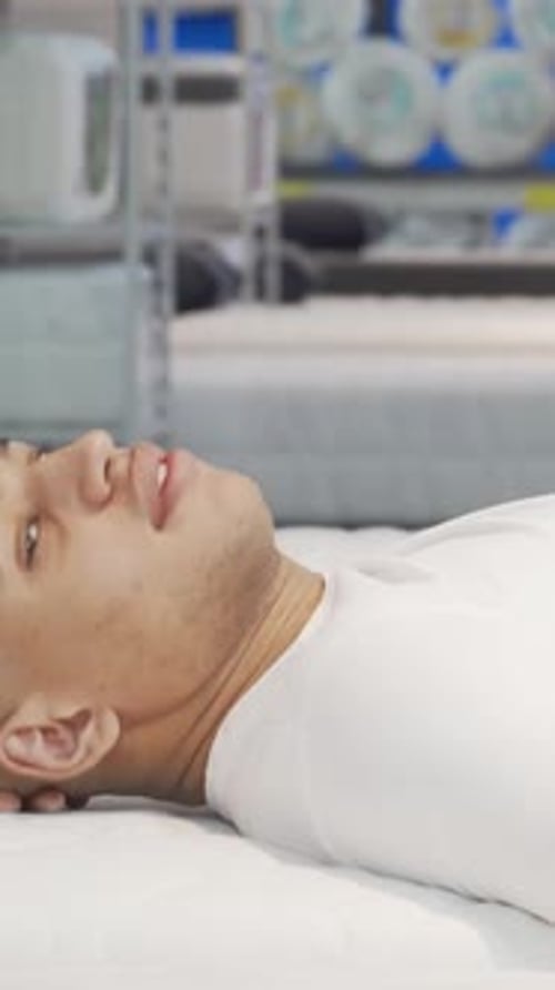 Joyful African Man Testing Orthopedic Mattress in a Stylish Furniture Store
