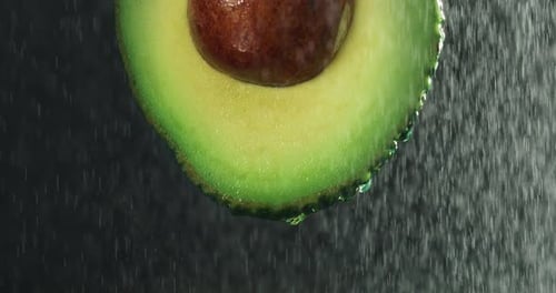 Cinematic macro shot of half raw fresh organic tropical green avocado fruit with falling water dro