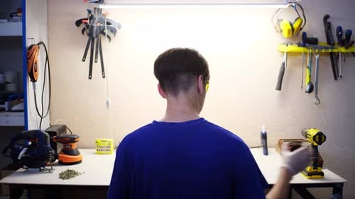 Young Man Takes Screws and Cordless Drill Sitting at Table